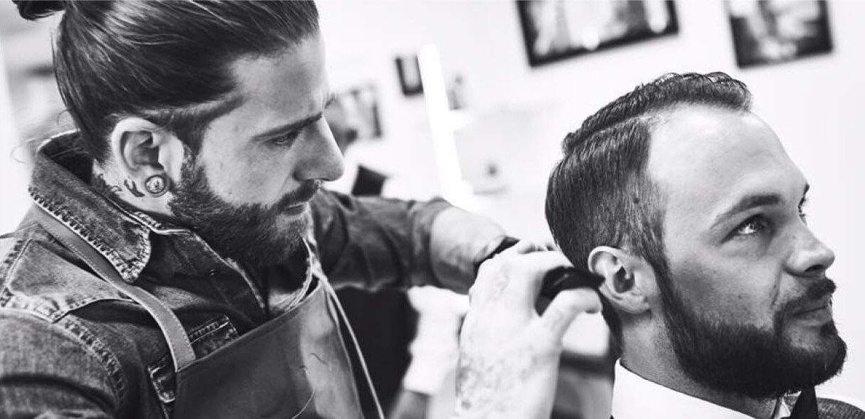 Mann mit Haarzopf und Bart frisiert Kunden